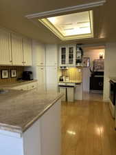 Kitchen featuring light hardwood / wood-style floors, a raised ceiling, light stone counters, and white cabinets