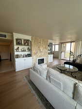 Living room featuring a stone fireplace, light hardwood / wood-style floors, built in features, and a textured ceiling