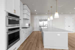 Kitchen featuring stainless steel appliances, pendant lighting, an island with sink, and white cabinets