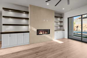 Unfurnished living room featuring light wood-type flooring, tile walls, a tiled fireplace, and ceiling fan