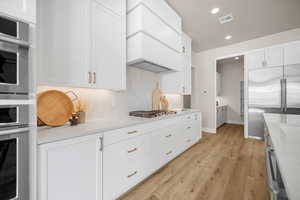 Kitchen featuring decorative backsplash, custom range hood, appliances with stainless steel finishes, light hardwood / wood-style floors, and white cabinetry