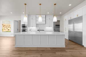 Kitchen featuring hanging light fixtures, light hardwood / wood-style floors, white cabinets, stainless steel appliances, and a center island with sink