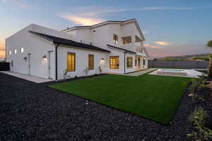 Back house at dusk with a balcony, a patio, a swimming pool, and a yard