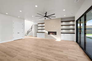 Unfurnished living room featuring ceiling fan, light wood-type flooring, and a tile fireplace