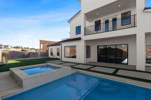 Back of house with a balcony, a patio, a yard, and an in ground hot tub