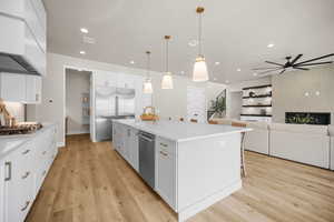 Kitchen featuring a kitchen island with sink, white cabinets, hanging light fixtures, appliances with stainless steel finishes, and light hardwood / wood-style floors