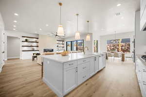 Kitchen featuring ceiling fan with notable chandelier, a kitchen island with sink, sink, pendant lighting, and light hardwood / wood-style floors