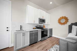 Kitchen with white cabinets, appliances with stainless steel finishes, light wood-type flooring, and sink