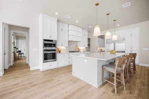 Kitchen with appliances with stainless steel finishes, a kitchen island with sink, decorative light fixtures, light hardwood / wood-style flooring, and white cabinetry