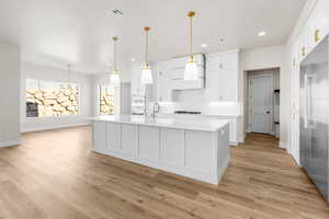 Kitchen with a kitchen island with sink, light hardwood / wood-style flooring, hanging light fixtures, and white cabinetry