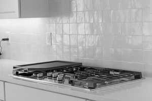 Room details featuring stainless steel gas stovetop, backsplash, white cabinetry, and light stone countertops