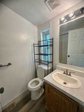 Bathroom with a textured ceiling, toilet, vanity, and wood-type flooring