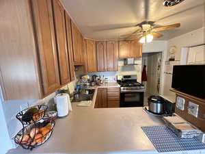 Kitchen featuring kitchen peninsula, ceiling fan, wall chimney exhaust hood, stainless steel gas range, and sink