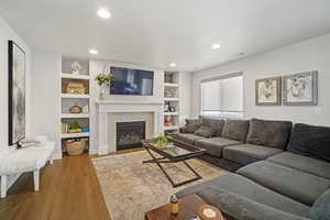 Living room featuring a fireplace, a textured ceiling, built in shelves, and light hardwood / wood-style floors