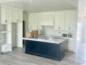 Kitchen featuring custom exhaust hood, light wood-type flooring, and a center island