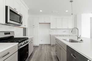 Kitchen with sink, hanging light fixtures, stainless steel appliances, light hardwood / wood-style flooring, and white cabinets