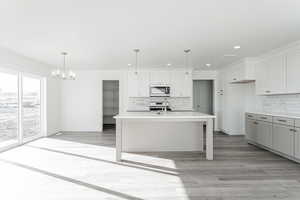 Kitchen featuring backsplash, white cabinetry, an island with sink, and hanging light fixtures