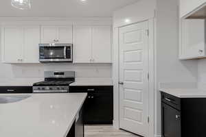 Kitchen with sink, light wood-type flooring, white cabinetry, and stainless steel appliances