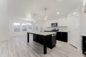 Kitchen with a center island with sink, white cabinets, appliances with stainless steel finishes, and light hardwood / wood-style flooring