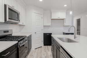 Kitchen with sink, appliances with stainless steel finishes, decorative light fixtures, white cabinets, and light wood-type flooring