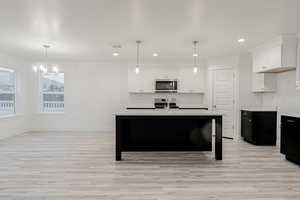 Kitchen with white cabinets, decorative light fixtures, light wood-type flooring, and stainless steel appliances