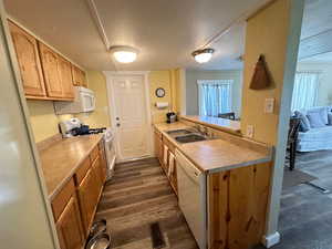 Kitchen featuring white appliances, sink, kitchen peninsula, a textured ceiling, and dark wood-type flooring