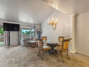 Carpeted dining room featuring a notable chandelier, ornate columns, a textured ceiling, and vaulted ceiling