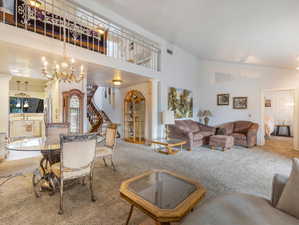 Living room with carpet flooring, a notable chandelier, decorative columns, and high vaulted ceiling