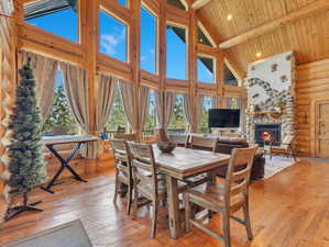 Dining area with log walls, wood ceiling, a stone fireplace, light wood-type flooring, and high vaulted ceiling