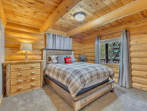 Bedroom featuring beam ceiling, light carpet, wood ceiling, and log walls