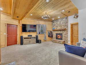 Carpeted living room featuring a fireplace, wood walls, a chandelier, and wooden ceiling