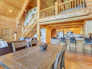 Dining space with beam ceiling, light hardwood / wood-style flooring, rustic walls, wood ceiling, and high vaulted ceiling