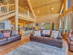 Living room featuring ceiling fan, high vaulted ceiling, rustic walls, light hardwood / wood-style floors, and wood ceiling