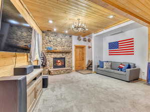 Living room featuring a stone fireplace, wood ceiling, and carpet floors