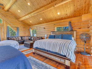 Bedroom with vaulted ceiling with beams, multiple windows, wood-type flooring, and log walls