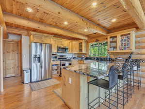 Kitchen with beamed ceiling, stainless steel appliances, light hardwood / wood-style floors, rustic walls, and wooden ceiling