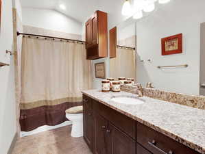 Bathroom with tile patterned flooring, vaulted ceiling, toilet, and vanity