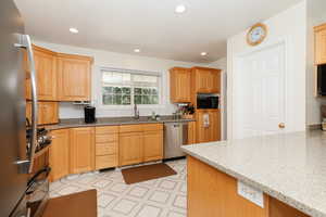 Kitchen with sink, light stone counters, appliances with stainless steel finishes, and light tile patterned floors