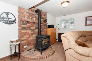 Living room featuring a wood stove, carpet flooring, and brick wall