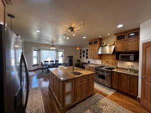 Kitchen with dark hardwood / wood-style floors, range hood, stainless steel appliances, sink, and ceiling fan