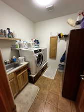 Clothes washing area with sink, washing machine and dryer, cabinets, and tile patterned floors