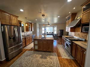 Kitchen with appliances with stainless steel finishes, sink, ceiling fan, pendant lighting, and a center island with sink