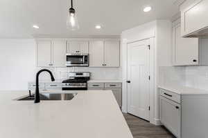 Kitchen with pendant lighting, dark wood-type flooring, sink, light stone counters, and stainless steel appliances