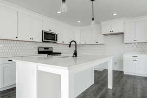 Kitchen featuring appliances with stainless steel finishes, white cabinetry, a kitchen island with sink, and pendant lighting