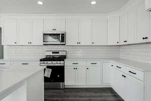 Kitchen with backsplash, white cabinetry, dark wood-type flooring, and appliances with stainless steel finishes