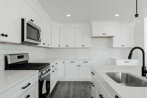 Kitchen featuring appliances with stainless steel finishes, dark hardwood / wood-style floors, white cabinetry, and hanging light fixtures