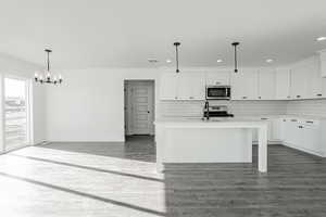 Kitchen with a center island with sink, pendant lighting, white cabinetry, and appliances with stainless steel finishes