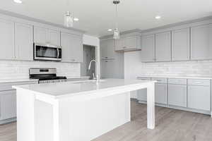 Kitchen with appliances with stainless steel finishes, light wood-type flooring, a textured ceiling, sink, and an island with sink