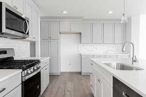 Kitchen with sink, hanging light fixtures, light hardwood / wood-style floors, decorative backsplash, and appliances with stainless steel finishes