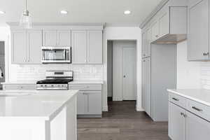 Kitchen with dark wood-type flooring, tasteful backsplash, pendant lighting, a textured ceiling, and appliances with stainless steel finishes